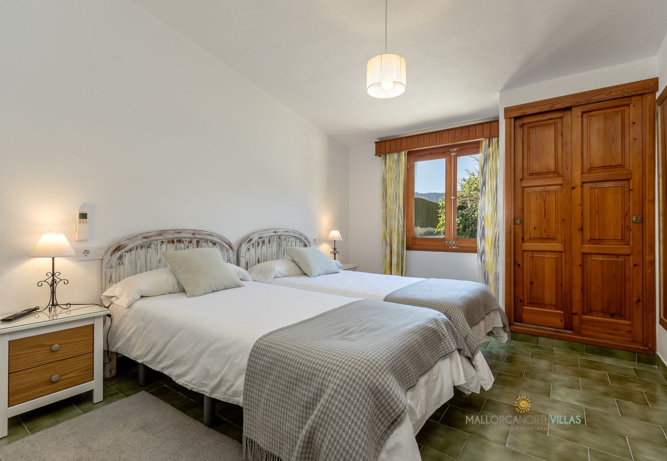 Dormitorio doble La Sort Llarga – Dos camas y armario Pollença Dormitorio con dos camas individuales, armario de madera y ventana al exterior en La Sort Llarga, Pollença