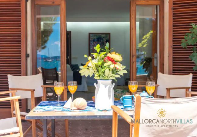 Terraza con acceso al salón en Puerto de Pollensa Mesa con flores y bebidas en la terraza con vistas hacia el salón interior.