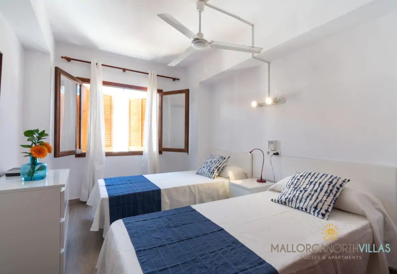 Dormitorio twin luminoso con ventilador Dos camas individuales con cubrepiés azules y ventana abierta con cortinas blancas