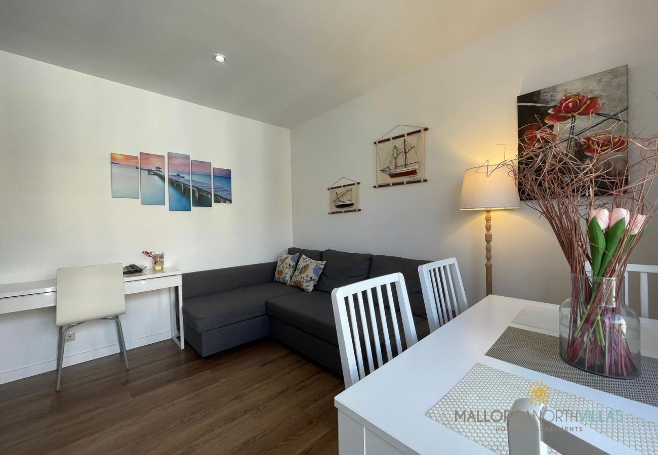 Acogedor apartamento con decoración moderna y estilo mediterráneo Sala de estar con sofá gris, mesa de comedor blanca, decoración náutica en las paredes y un escritorio con silla blanca.