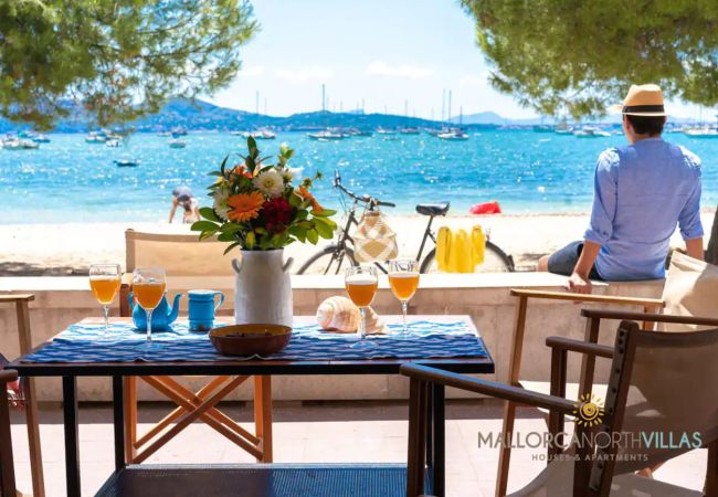 Meerblick-Terrasse in Puerto Pollensa Tisch mit Getränken und Blumen auf der Terrasse mit Blick auf Strand und Meer.