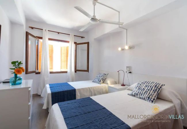Helles Twin-Schlafzimmer mit Deckenventilator Zwei Einzelbetten mit blauen Läufern und geöffnetem Fenster mit weißen Vorhängen