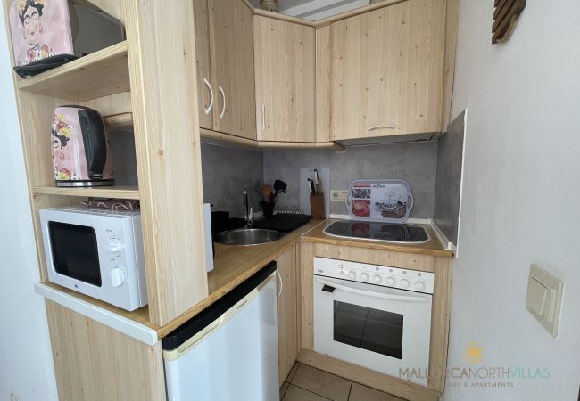 Kompakte Küche mit wichtigen Geräten Kleine Küche mit Holzschränken, Kochfeld, Backofen, Spüle, Mikrowelle und Kühlschrank.