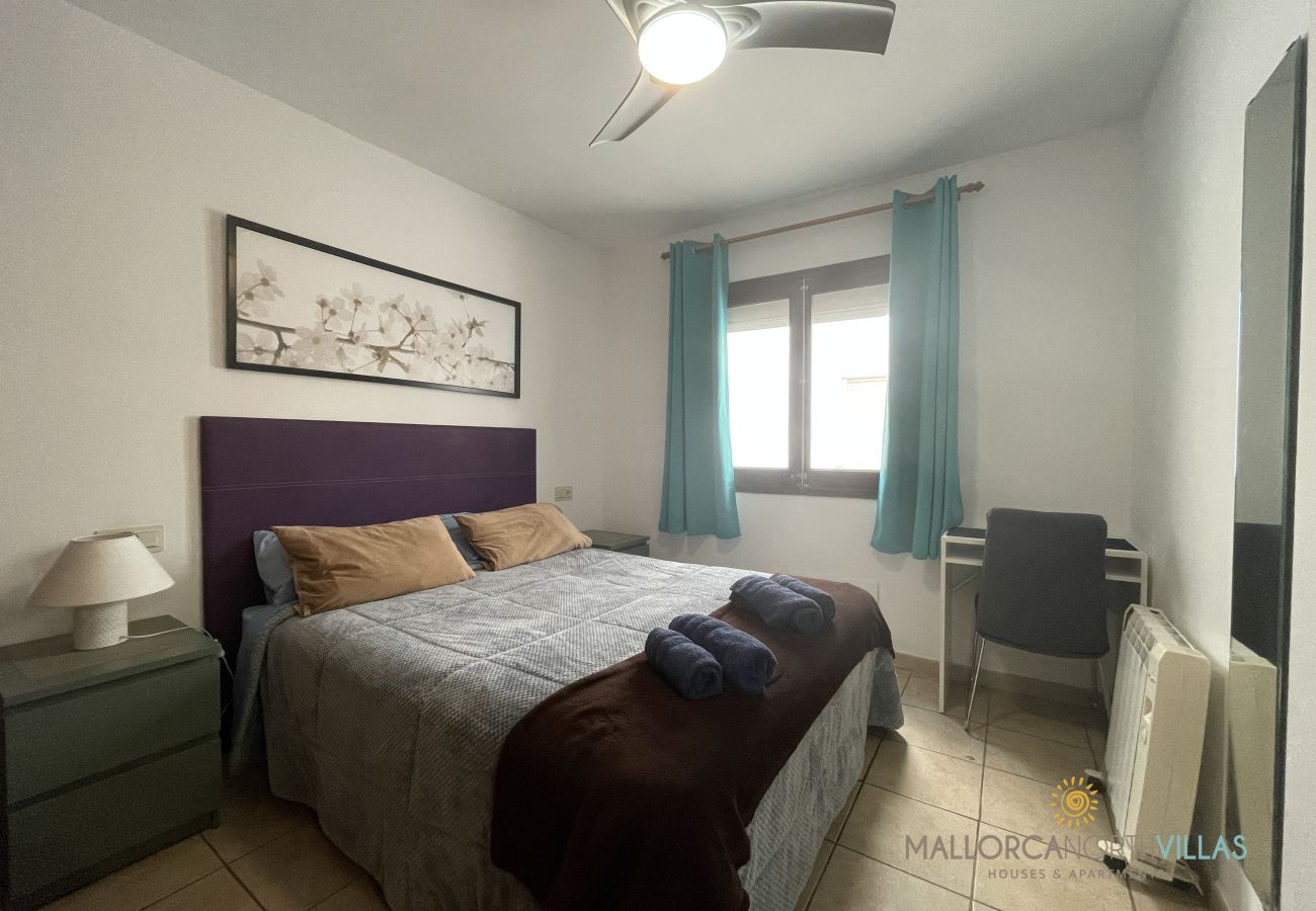 Schlafzimmer mit Doppelbett und hellem Fenster Schlafzimmer mit Doppelbett in Blau- und Brauntönen, lila Kopfteil, Fenster mit türkisfarbenen Vorhängen und Schreibtisch.