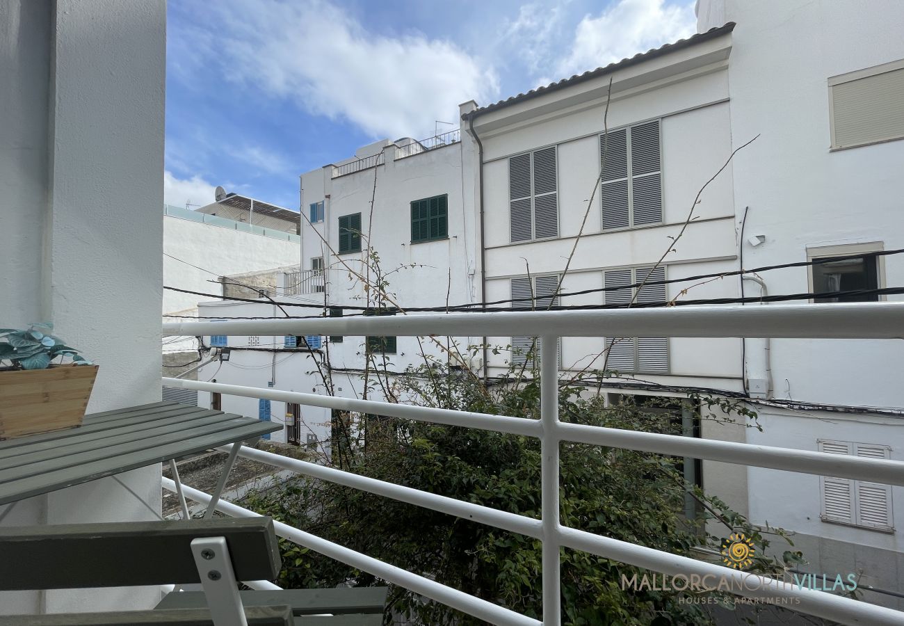 Balcony overlooking an inner courtyard Balcony with a white railing and a folding table, overlooking an inner courtyard surrounded by white buildings with shutters.